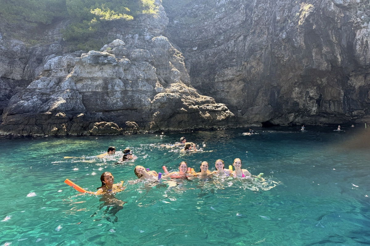 Group swimming with pool noodles in turquoise water at a swim stop on a Dubrovnik Blue Cave boat tour